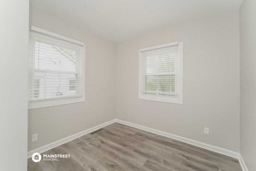 a bedroom with wood flooring and two windows