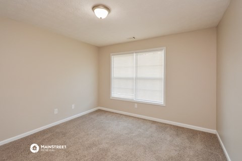 the spacious bedroom with carpet and a large window