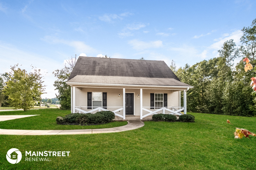 a small white house with a porch on a green lawn