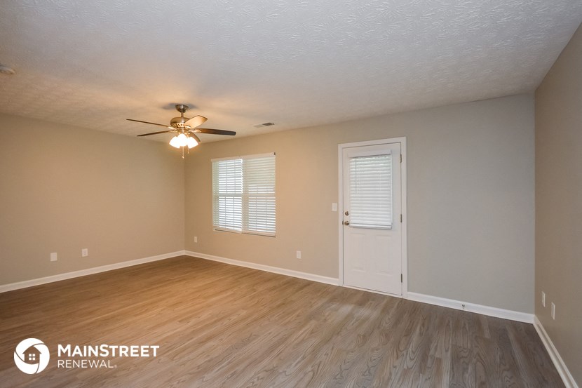 the spacious living room with wood flooring and a ceiling fan