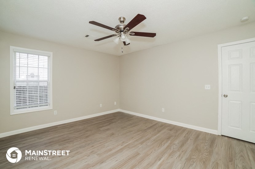 the spacious living room with wood flooring and a ceiling fan