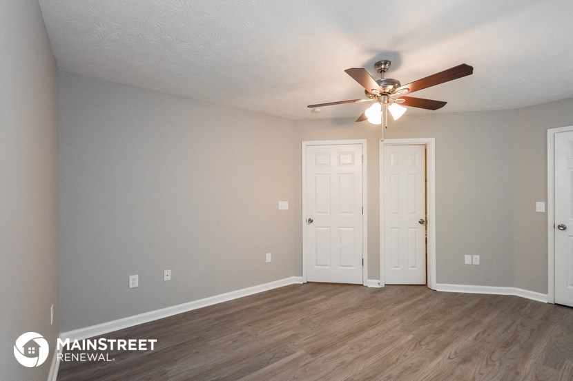 the spacious living room with ceiling fan and white doors