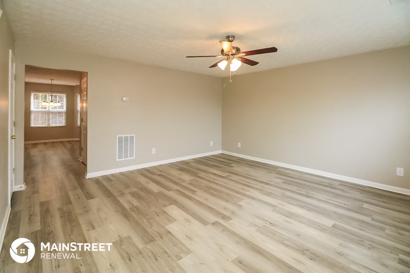 the spacious living room with wood flooring and a ceiling fan