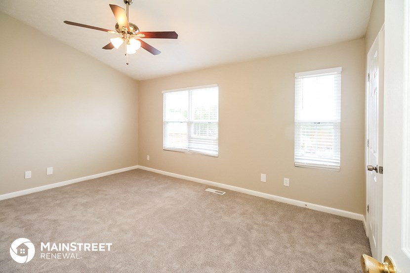 an empty room with a ceiling fan and two windows