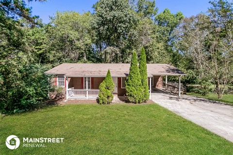 a small red brick house with a lawn and trees