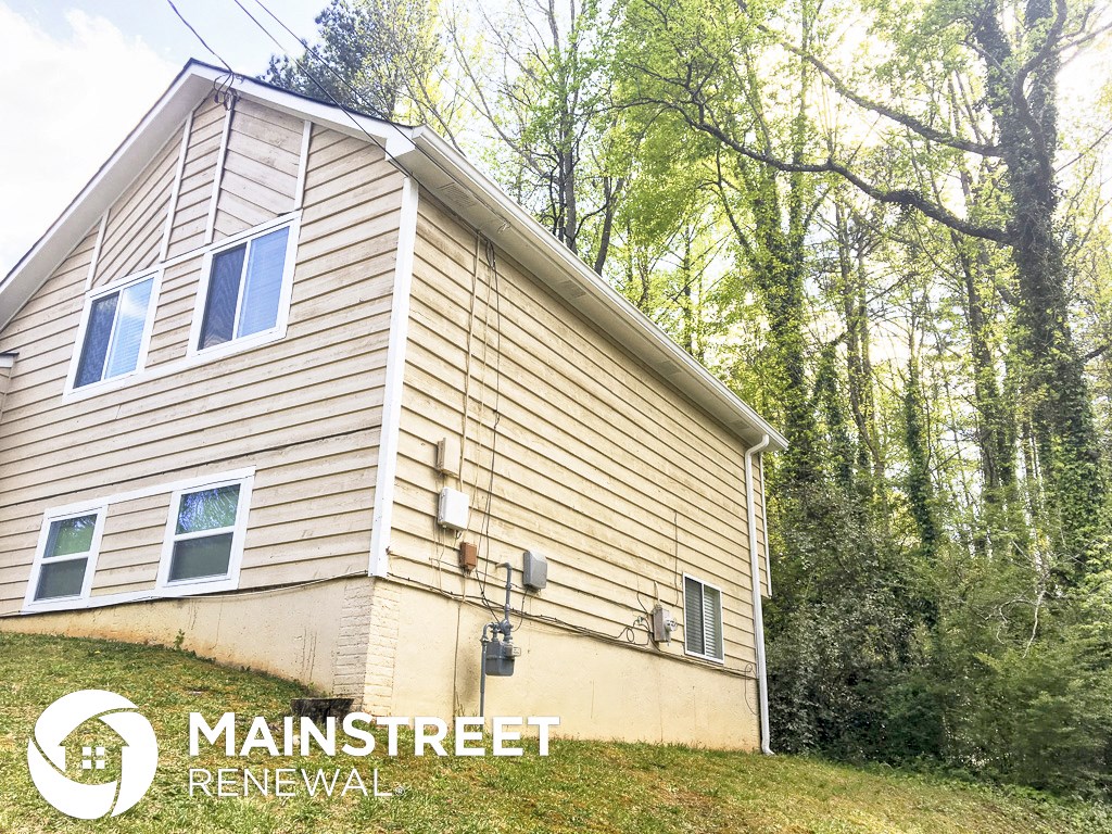 a white house with wood siding on a hill with trees