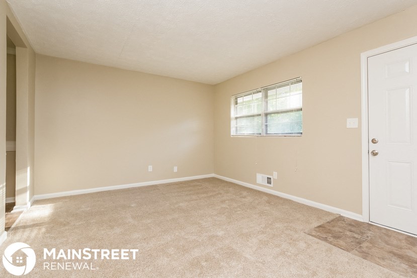 the spacious living room with carpeted flooring and a white door