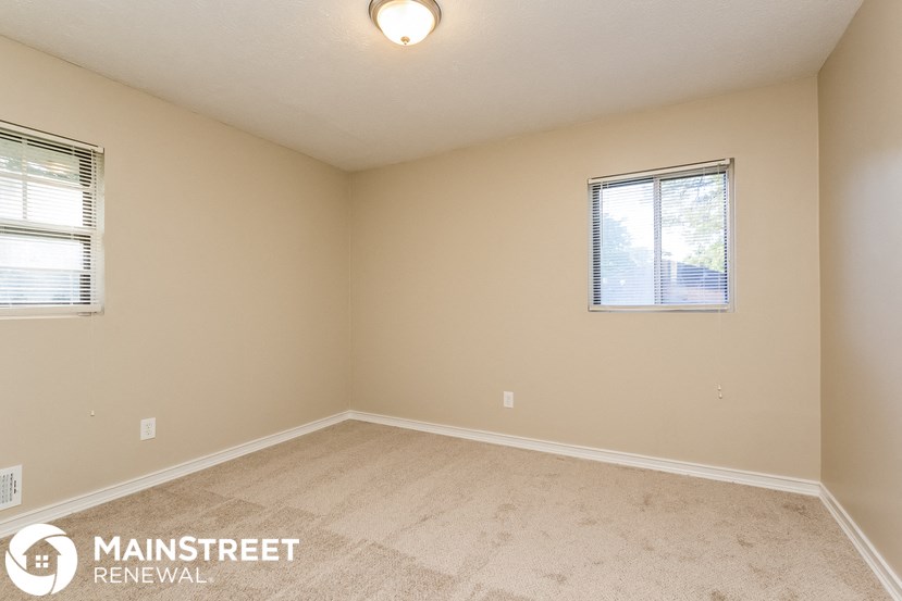 the spacious living room with carpeted floors and two windows