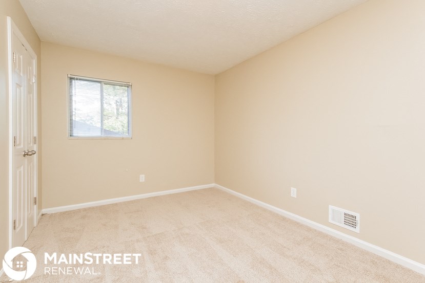 a spacious bedroom with beige carpet and a window