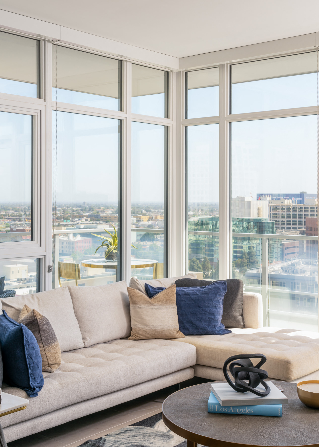 A living room with a couch and a table in front of large windows overlooking a cityscape.