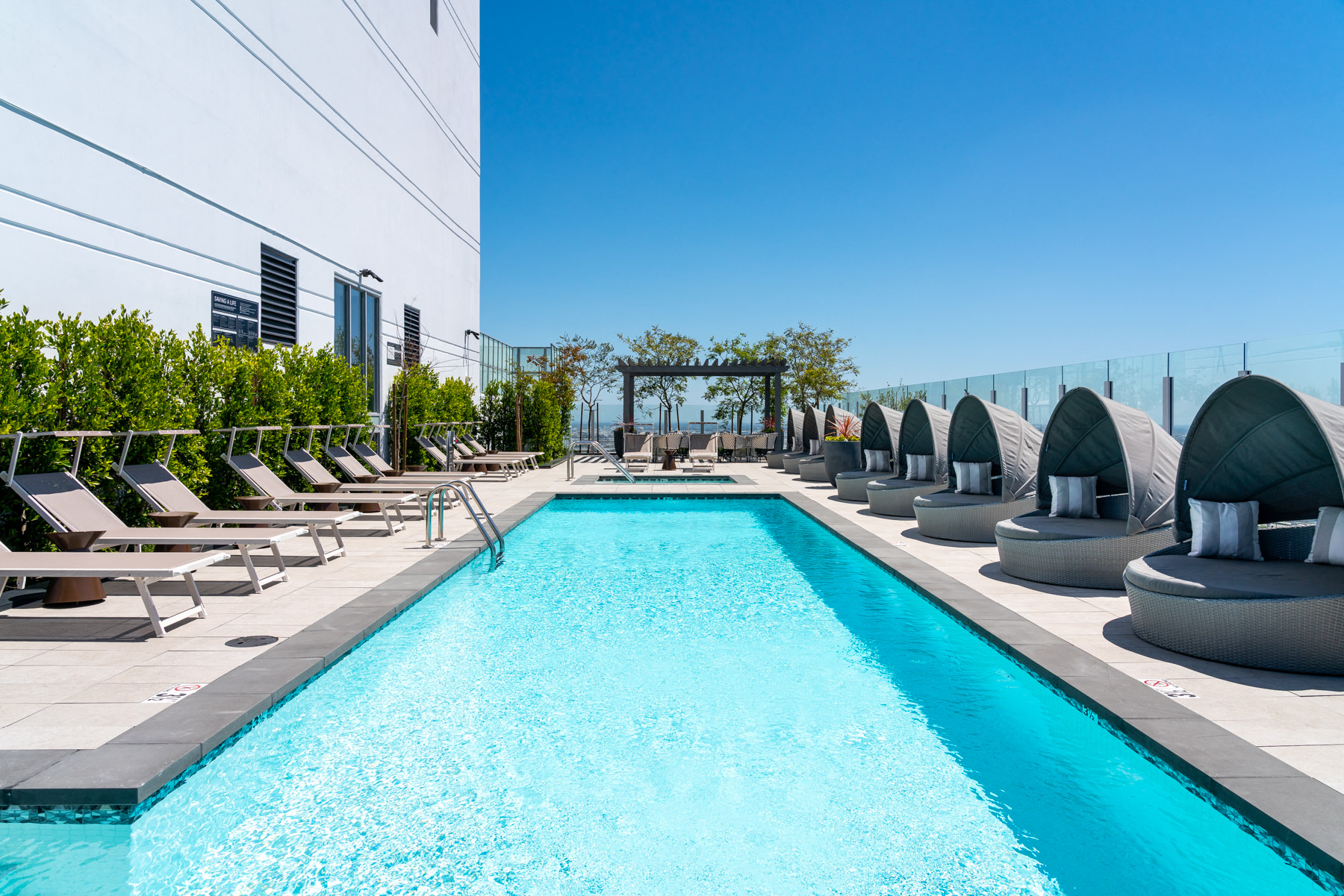 A long rectangular pool with a blue tinted water surrounded by sun loungers and umbrellas.