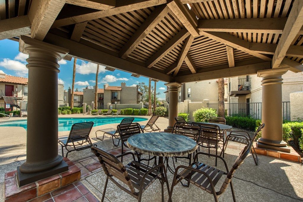 a covered patio with tables and chairs next to a swimming pool