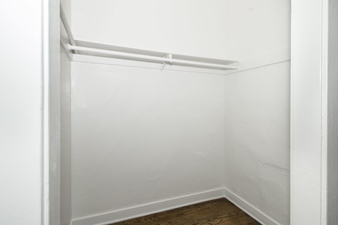 A white closet with a wooden floor and a white rail.