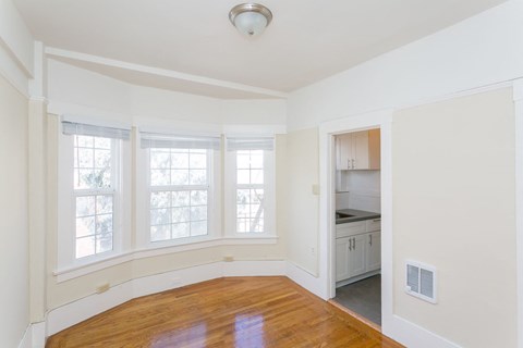 A room with a wooden floor and a kitchen area in the background.