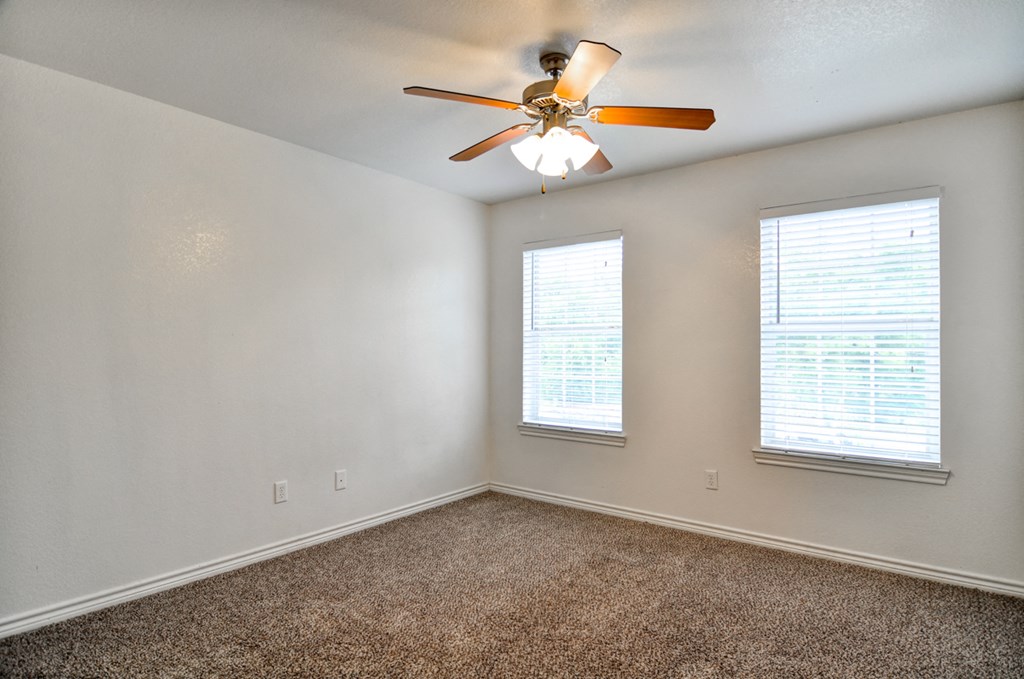 an empty room with a ceiling fan and two windows