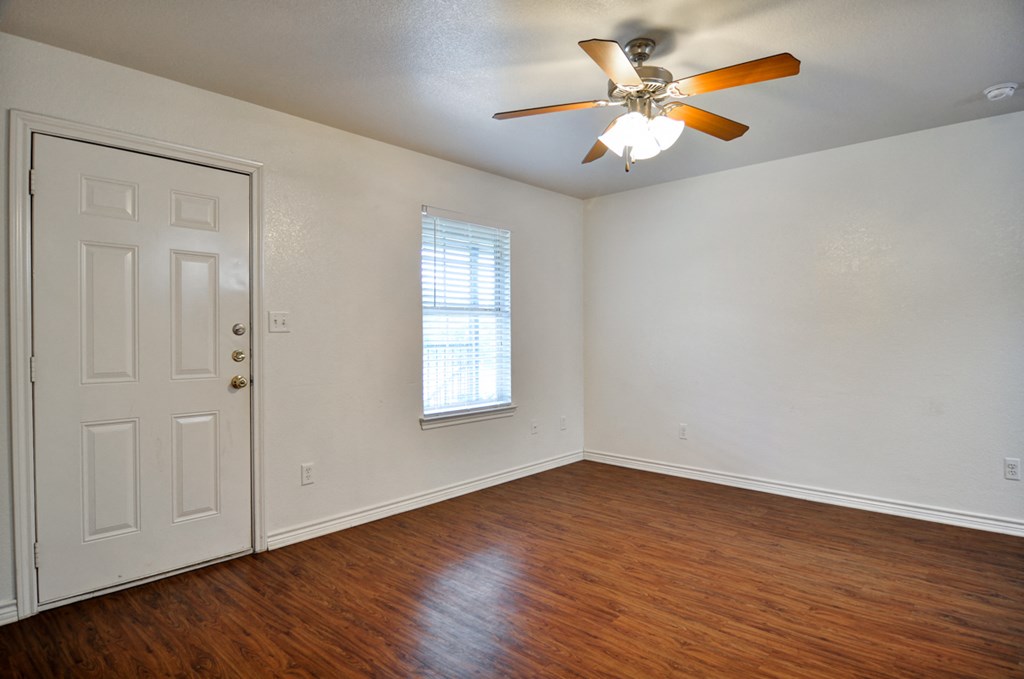 an empty living room with wood floors and a ceiling fan