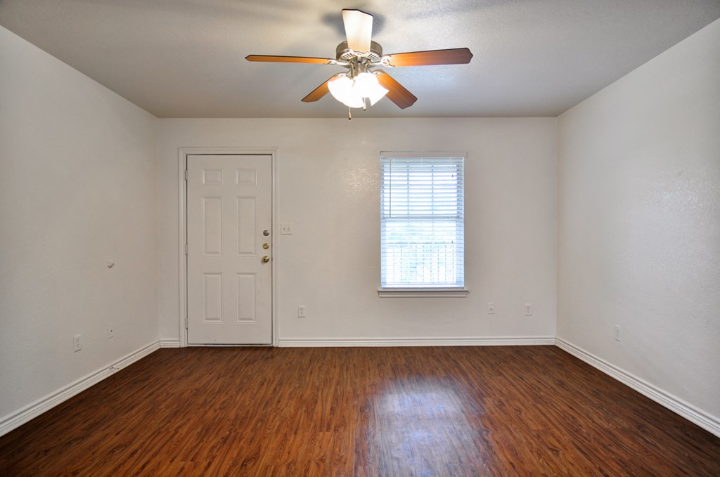 an empty living room with wood floors and a ceiling fan
