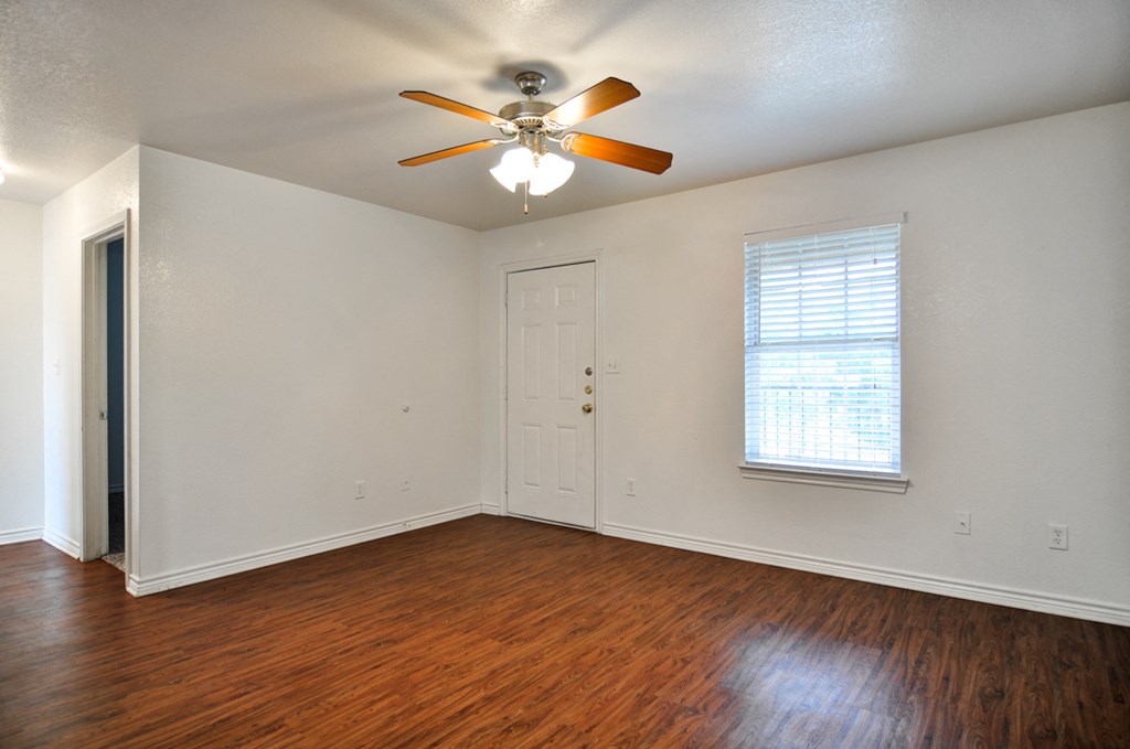 an empty living room with wood floors and a ceiling fan