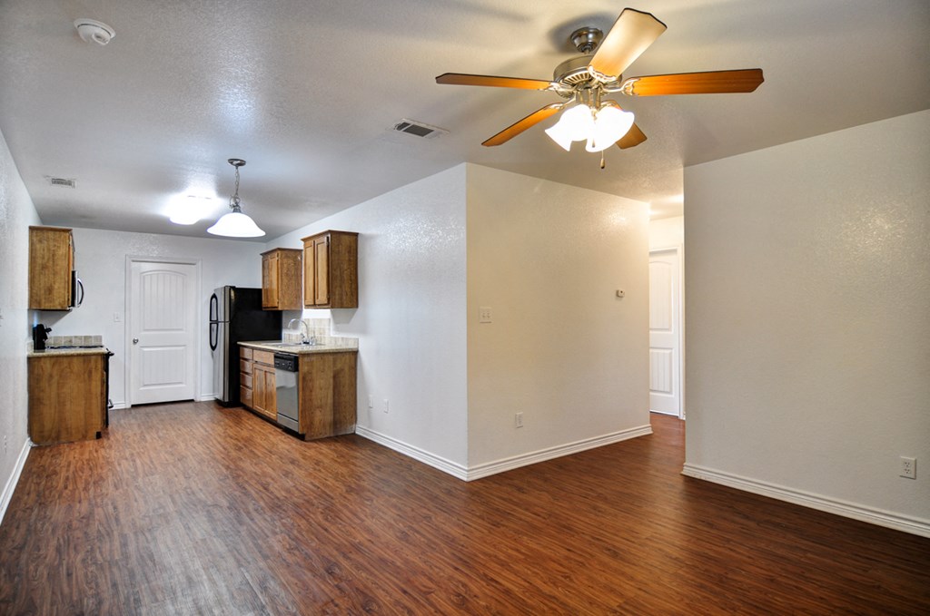 an empty living room with a ceiling fan and a kitchen