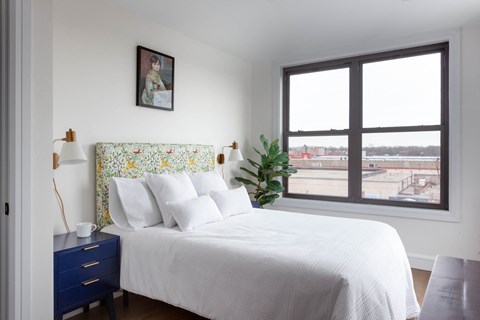 A bedroom with a large bed and a window overlooking a cityscape.