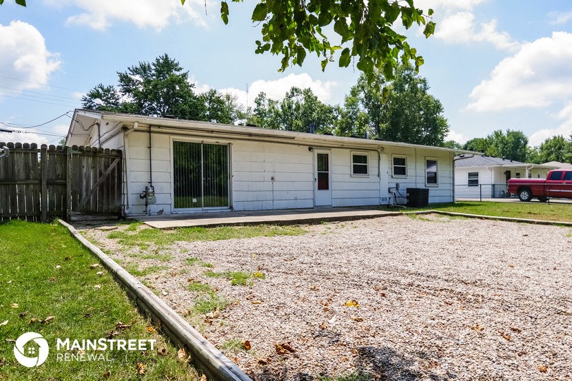 a small white house with a gravel driveway and a tree