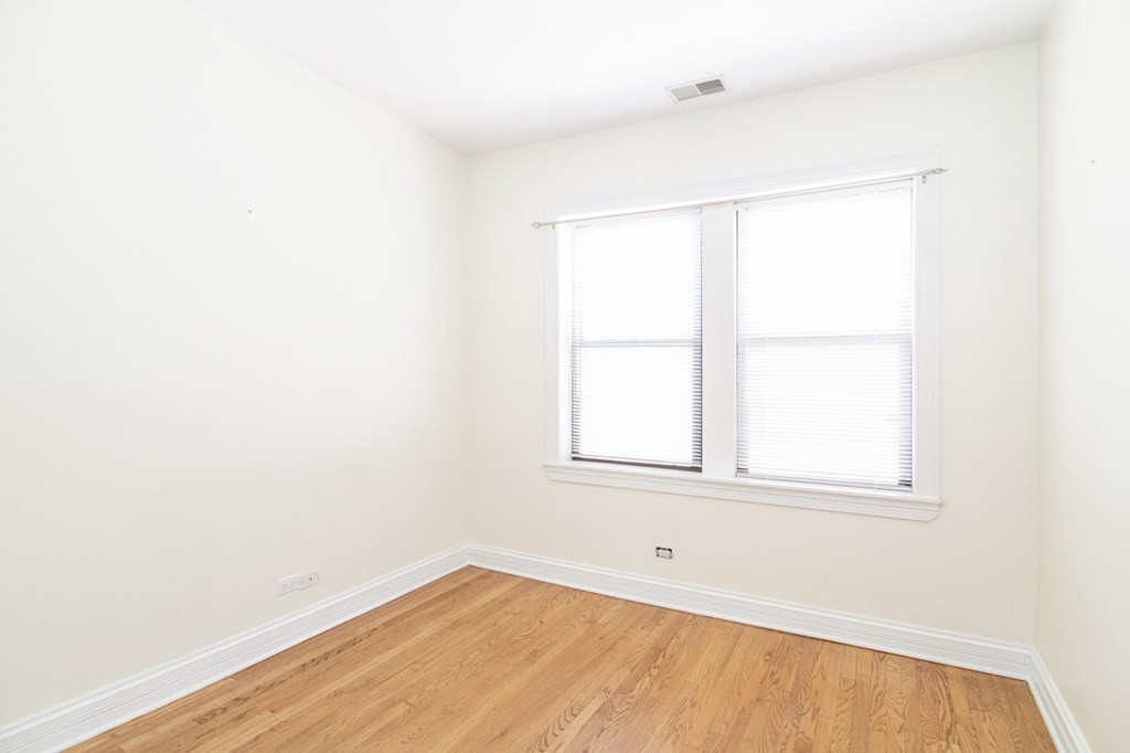 a bedroom with white walls and a window and wood floors