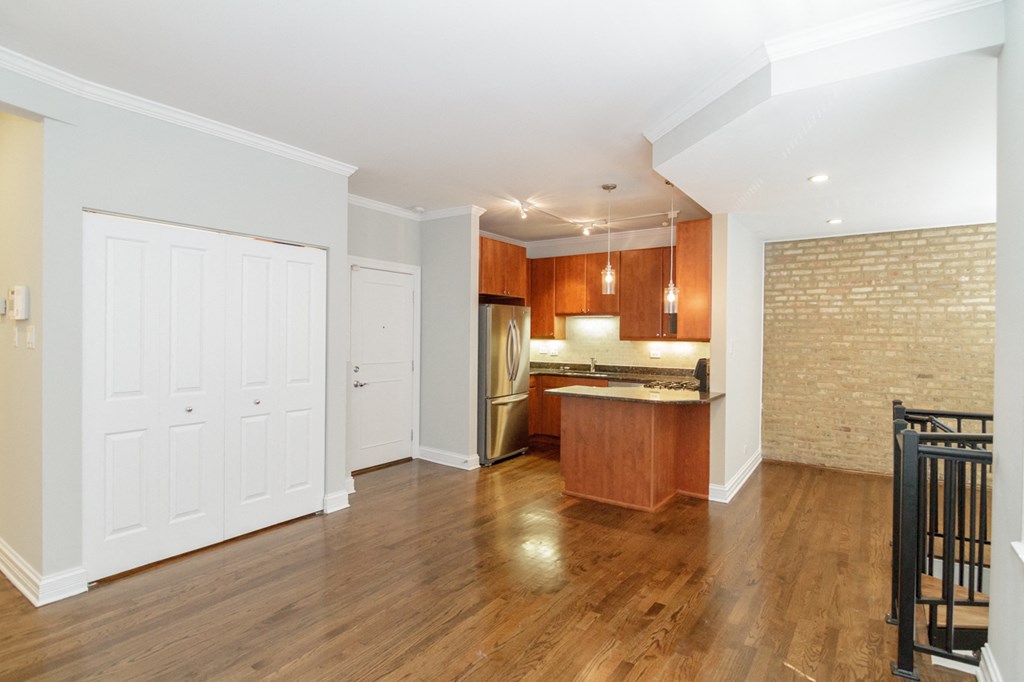 an empty living room with a kitchen with wood flooring