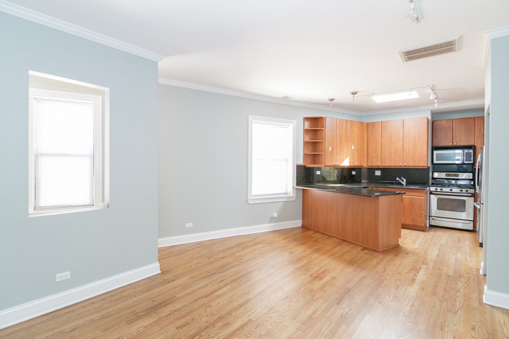 an empty living room with a kitchen with wood floors and wooden cabinets