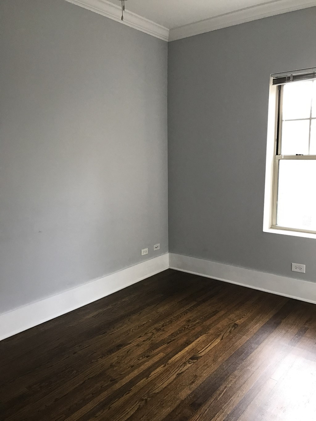 an empty room with gray walls and wooden floors and a window