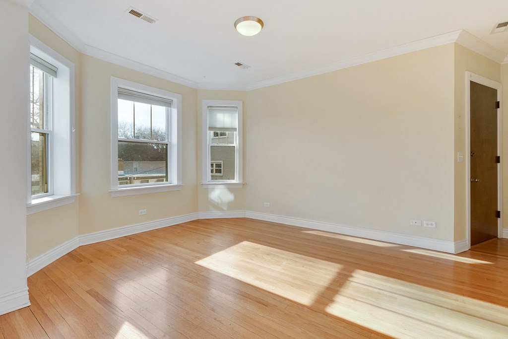 an empty living room with a hardwood floor and three windows