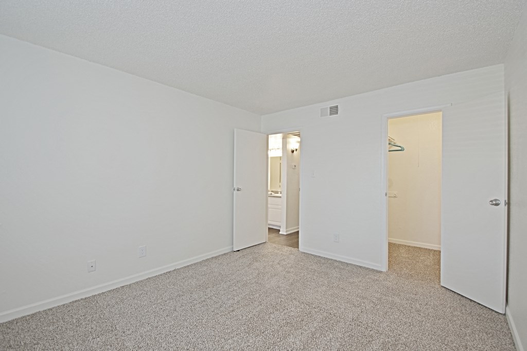 the spacious living room of an apartment with carpeting and white walls