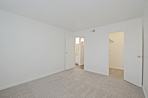 the spacious living room of an apartment with carpeting and white walls