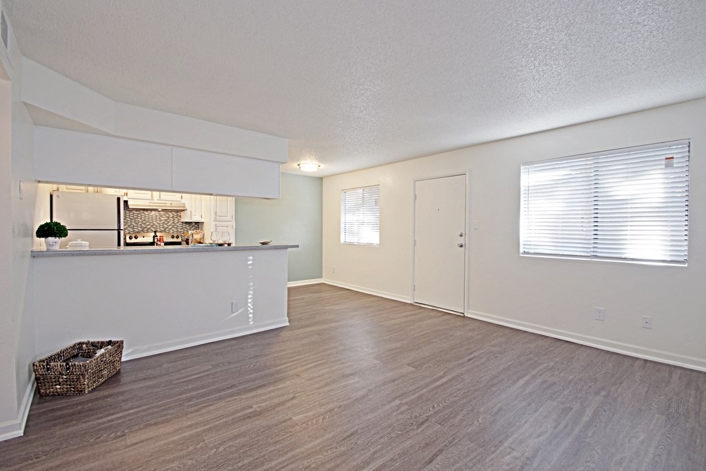 the living room and kitchen of an apartment with white walls and wood flooring
