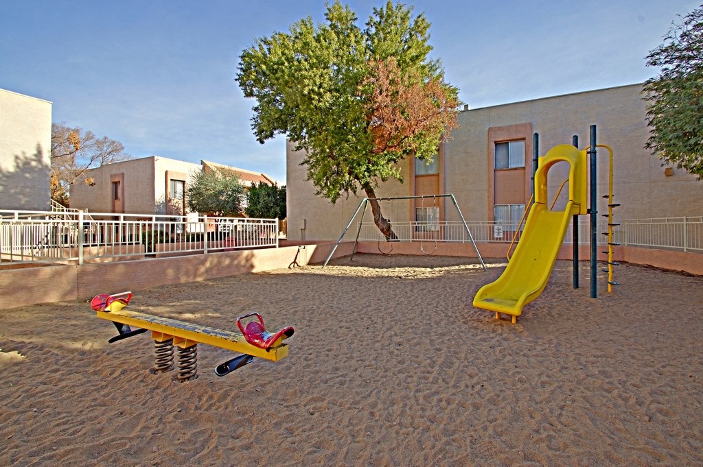 a playground with a slide and a seesaw in front of a building