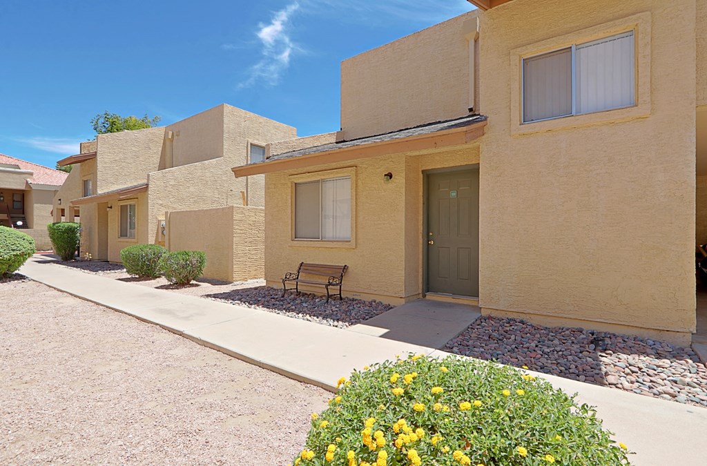 a bench sits in front of a tan building with a door