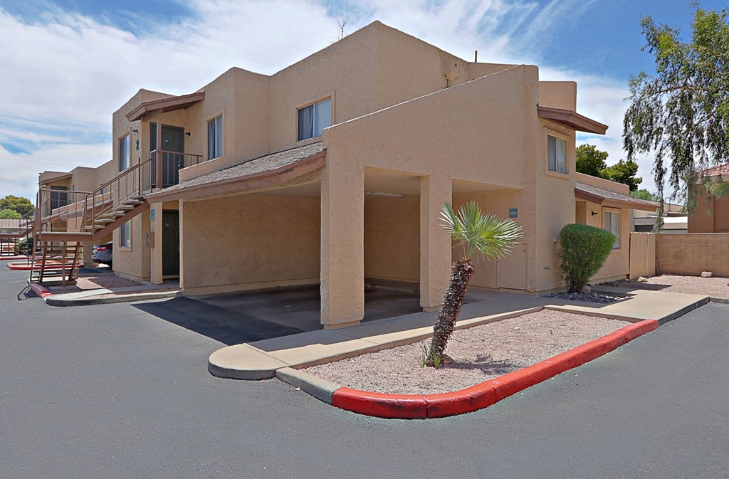 an empty parking lot in front of a tan building with a palm tree