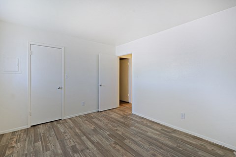 a bedroom with white walls and wood flooring and a closet