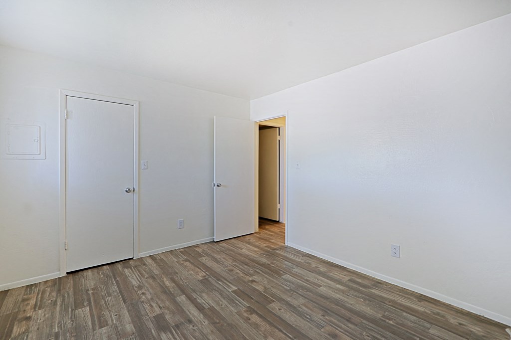 a bedroom with white walls and wood flooring and a closet