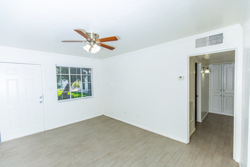 an empty living room with a ceiling fan and a door to a hallway