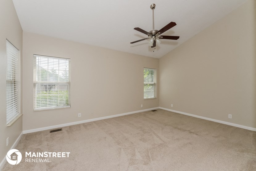 the spacious living room with carpet and ceiling fan