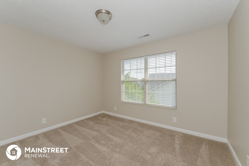 the spacious living room with a large window and beige carpeting