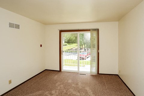 A room with a carpeted floor and a sliding glass door leading to a parking lot.