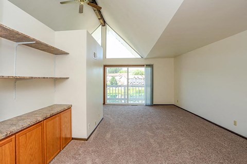 A room with a carpeted floor and a slanted ceiling with a fan.