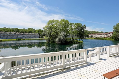 A wooden deck overlooks a body of water with a bench and a railing.