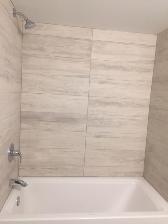 a white bath tub in a tiled bathroom with a shower