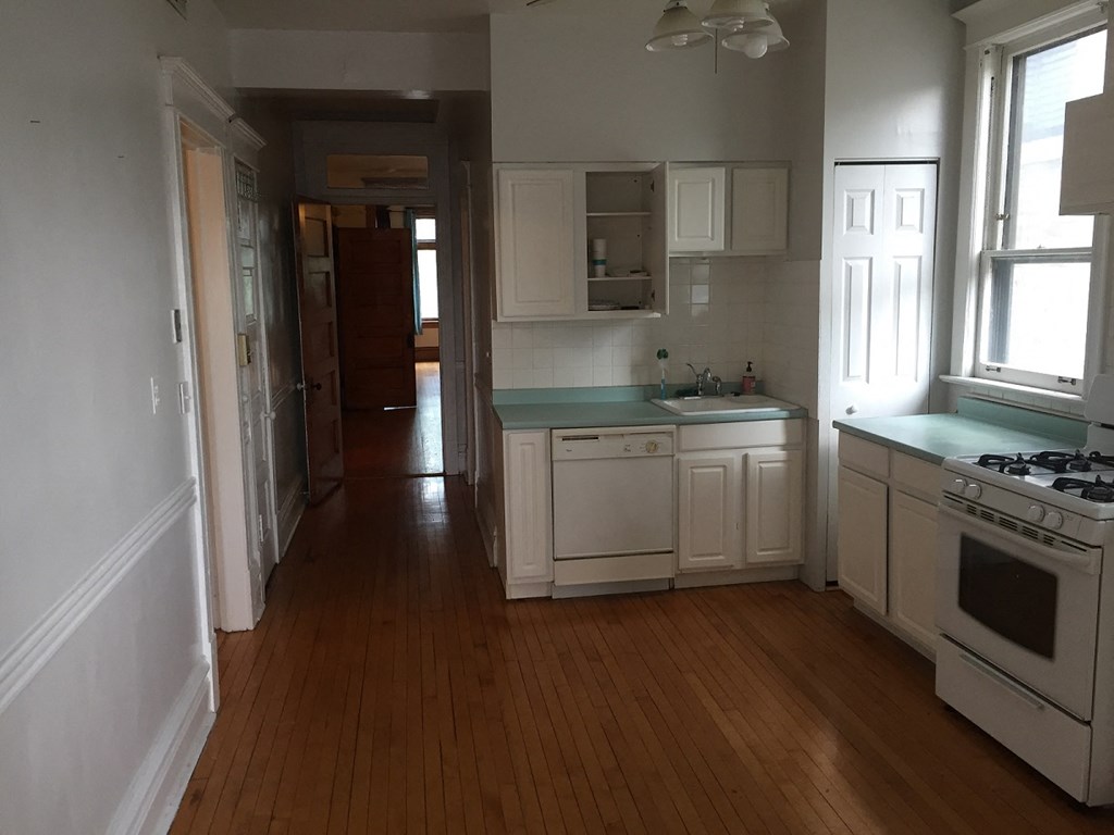 an empty kitchen with wooden floors and white cabinets