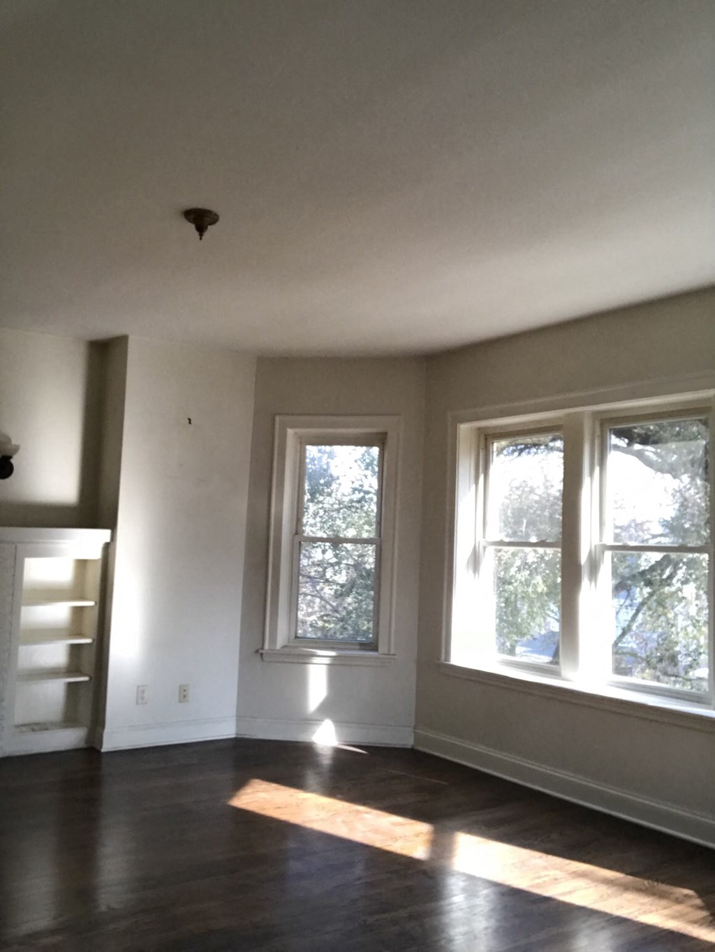 a living room with three windows and a hard wood floor