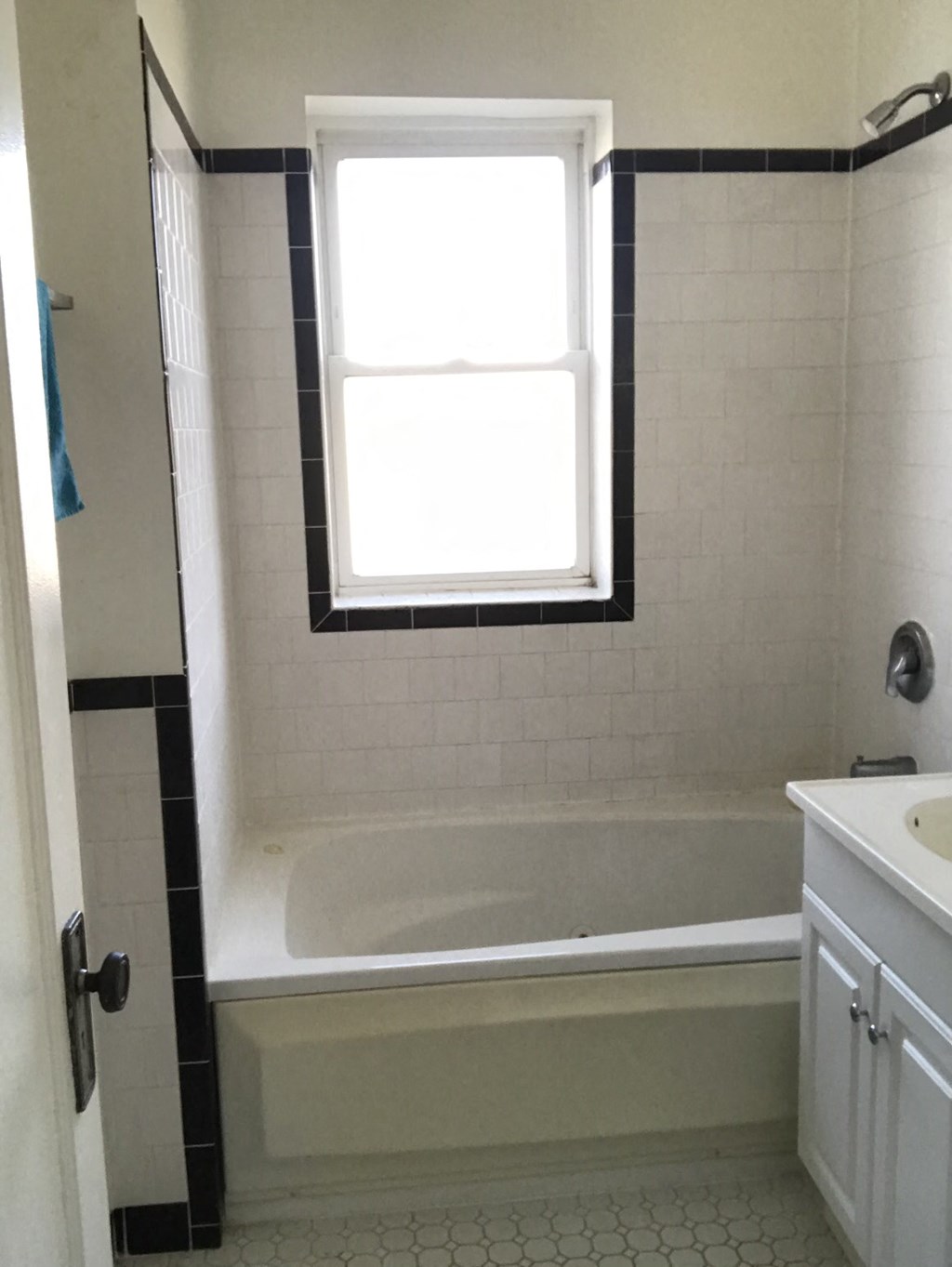 a white tiled bathroom with a tub and a window