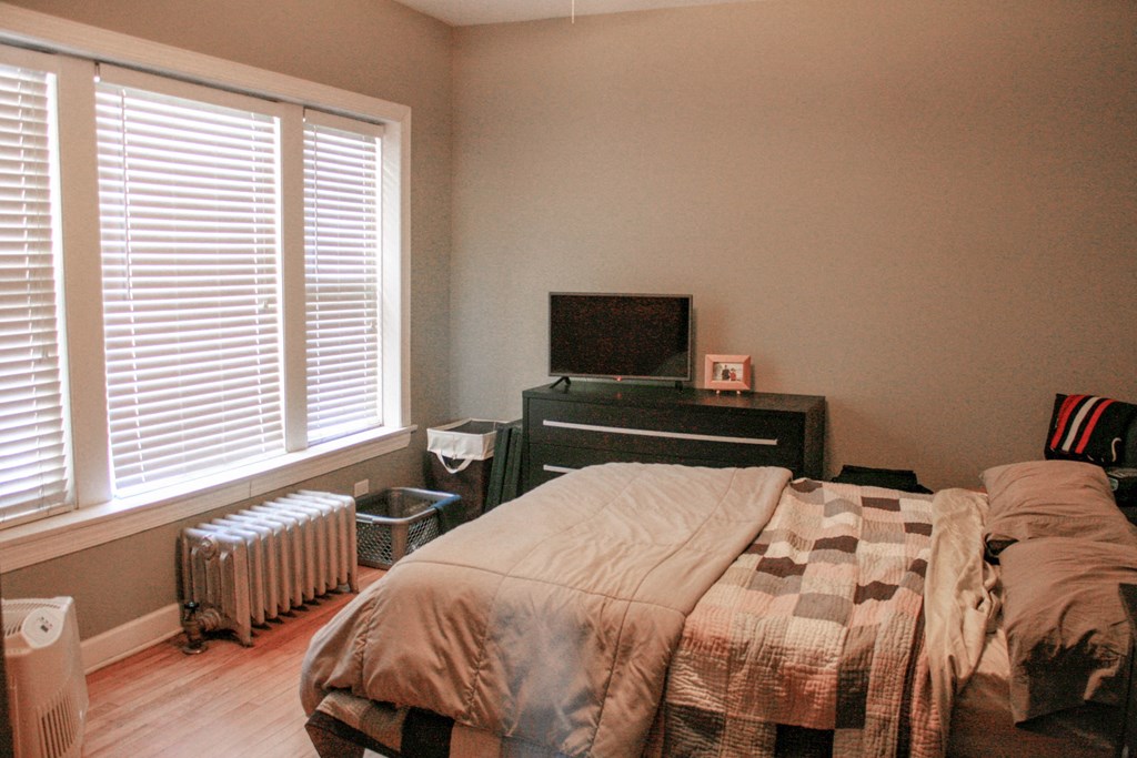 a bedroom with a bed and a dresser and two windows