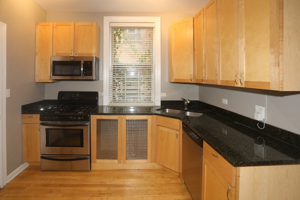a kitchen with black countertops and wooden cabinets and a window